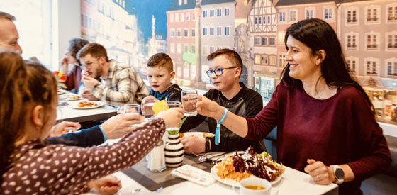 Eine Familie im Restaurant der Jugendherberge Trier. Die Eltern sitzen mit den Kindern an Tisch und stoßen mit gefüllten Glasen an.